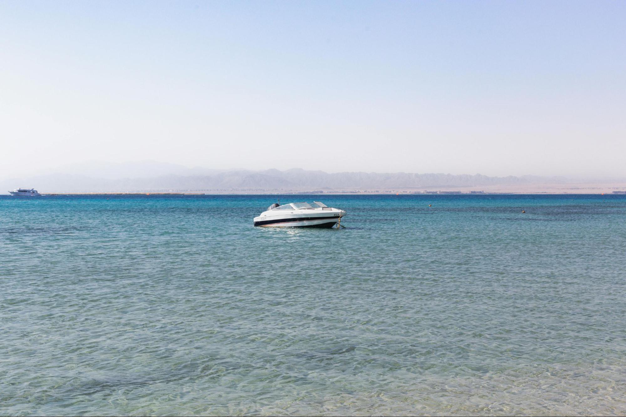 A white speedboat with a black stripe sits anchored on calm, clear turquoise water.