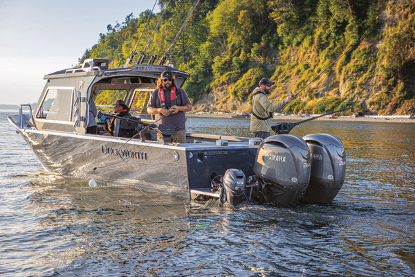 Two people fish from a Duckworth boat with Yamaha outboards near a forested shoreline in warm evening light.