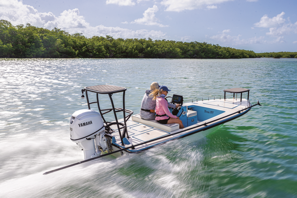 Two people cruise through coastal waters in a shallow-water fishing skiff powered by a Yamaha outboard motor.