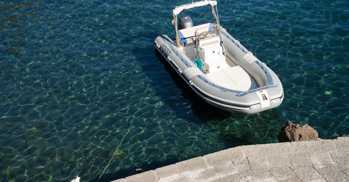 An empty, small, white, and luxurious inflatable boat is tied to a small rock near a platform on crystal blue water. An empty, small, white, and luxurious inflatable boat is tied to a small rock near a platform on crystal blue water.