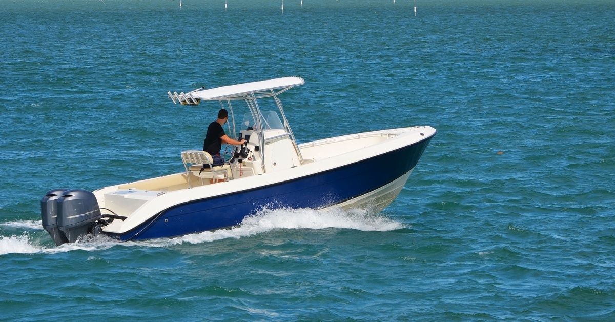 A guy in a black shirt is operating a small, open white-and-blue sport fishing boat powered by two outboard engines.