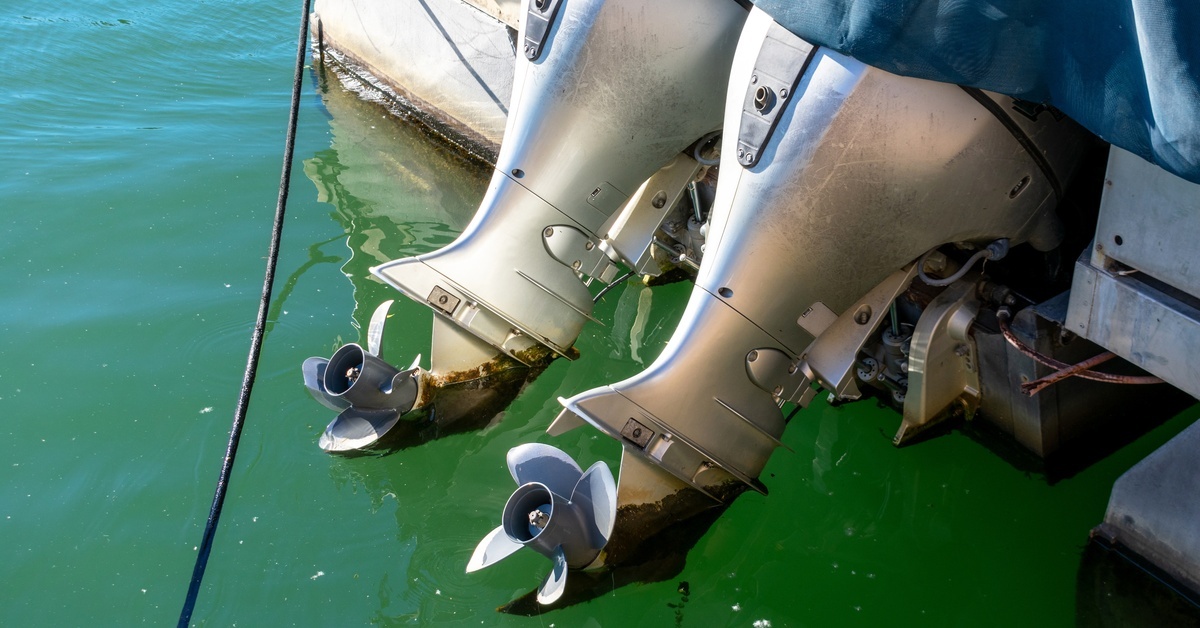 A close-up of two powerful outboard engines on the boat. The propeller from the motor is out of the green-blue water.