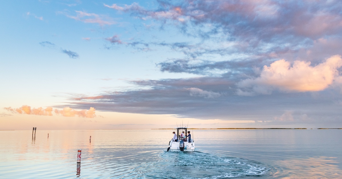 A Beginner’s Guide to Navigating Tides and Currents A boat heads out on the calm ocean on a fishing trip as the sun rises. There are a few clouds in the sky.