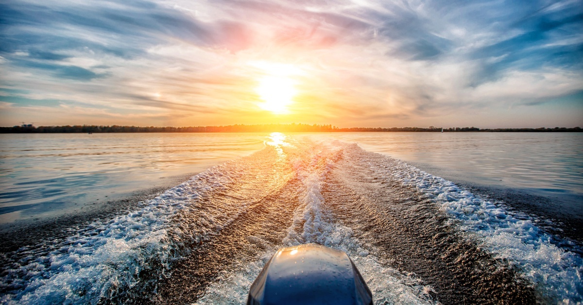 A running outboard engine is creating a beautiful wake on the water behind the boat's stern while the sun sets.