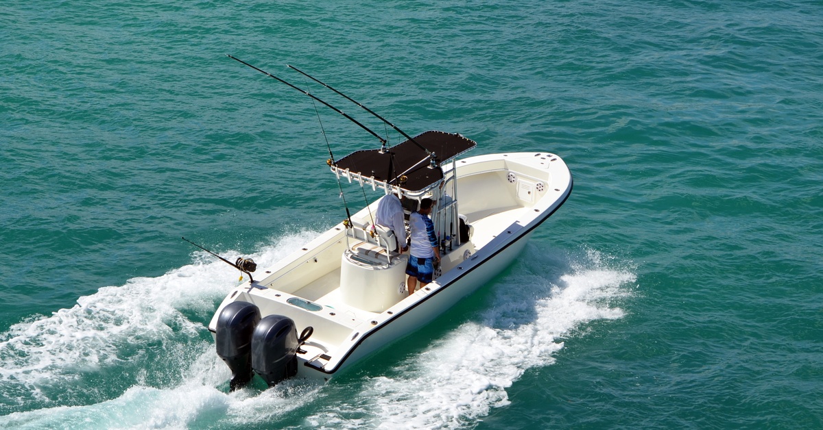 A sport fishing boat with a black covering over the center console, powered by two outboard engines.