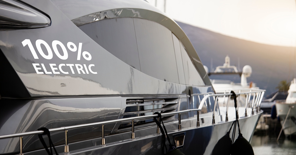 Comparing Electric vs. Gas Boating: What You Should Know A close-up of a gray-black luxury yacht, that's docked on the water and has a "100% electric" decal on the side.