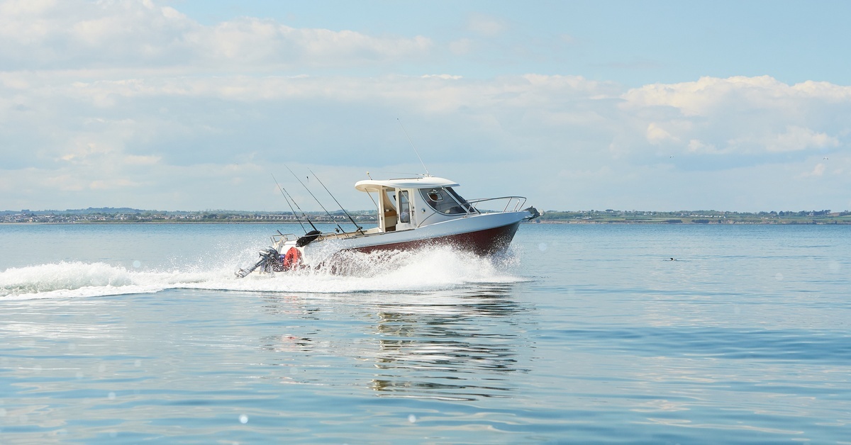 Spirit Outboard Motors: How Long Can They Last? A large, white motorboat moving quickly through the water, creating waves along its path. White clouds billow in the distance.
