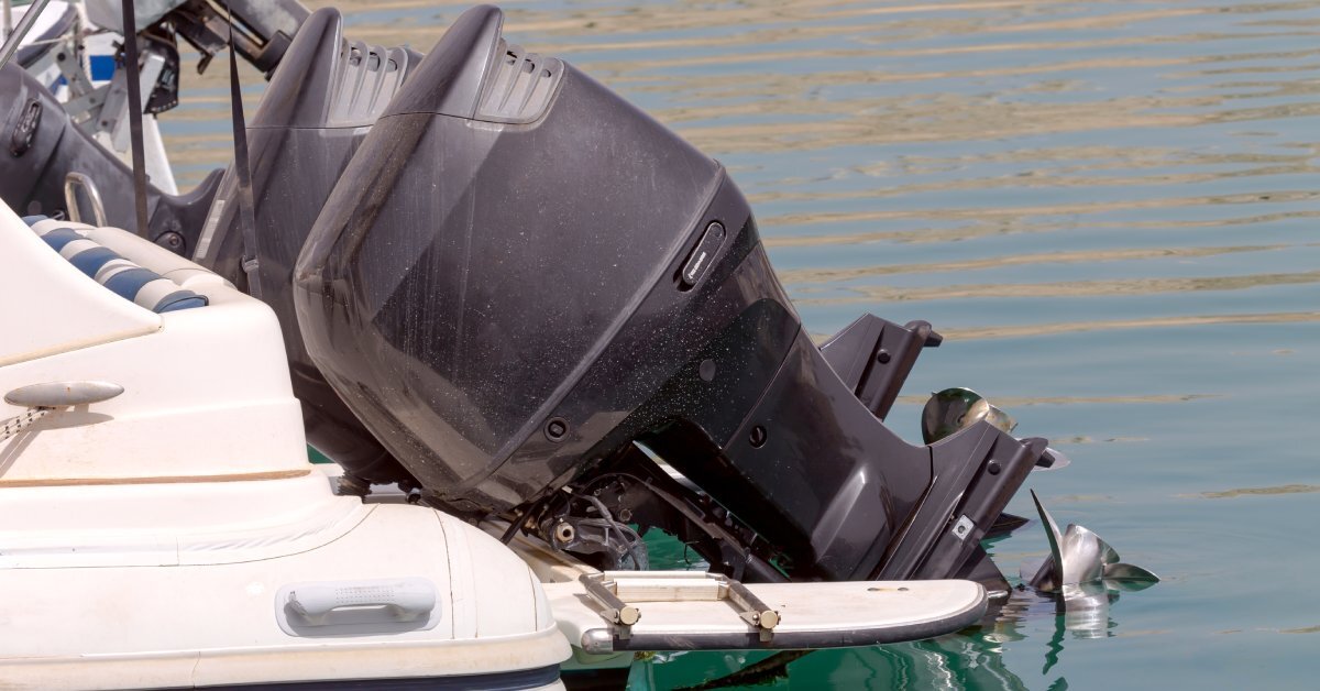 A black outboard motor at the back end of a boat, with the tail end of the motor sitting in the water.