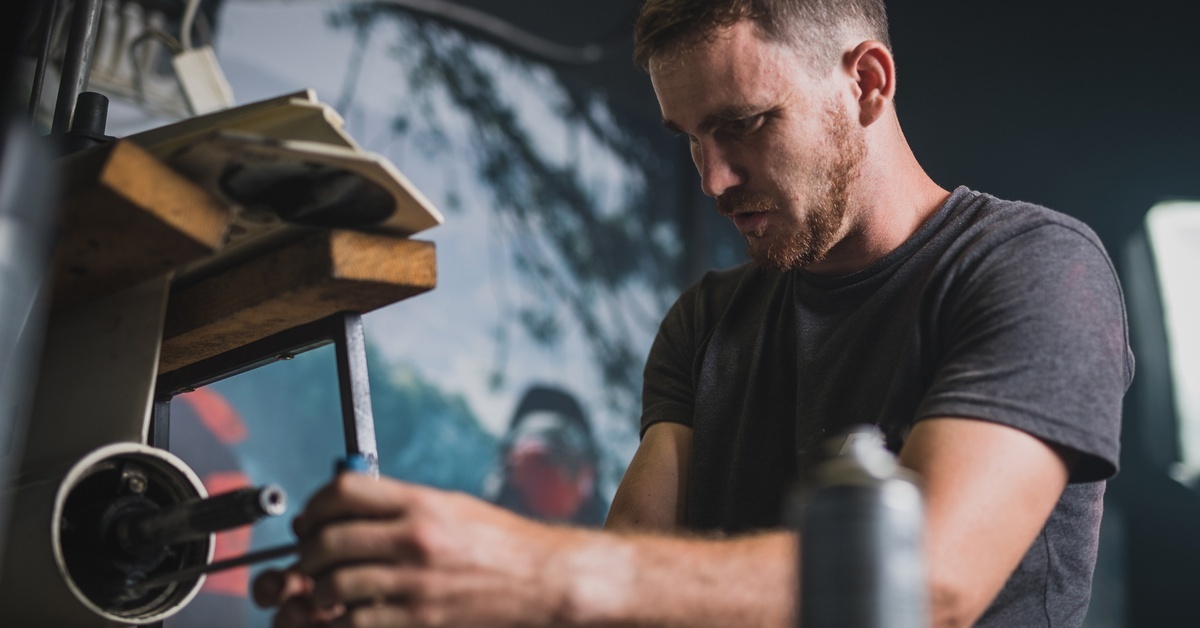 A man works in a dimly lit workshop, using a spanner to loosen a screw on a component of an outboard ship engine. A man works in a dimly lit workshop, using a spanner to loosen a screw on a component of an outboard ship engine.