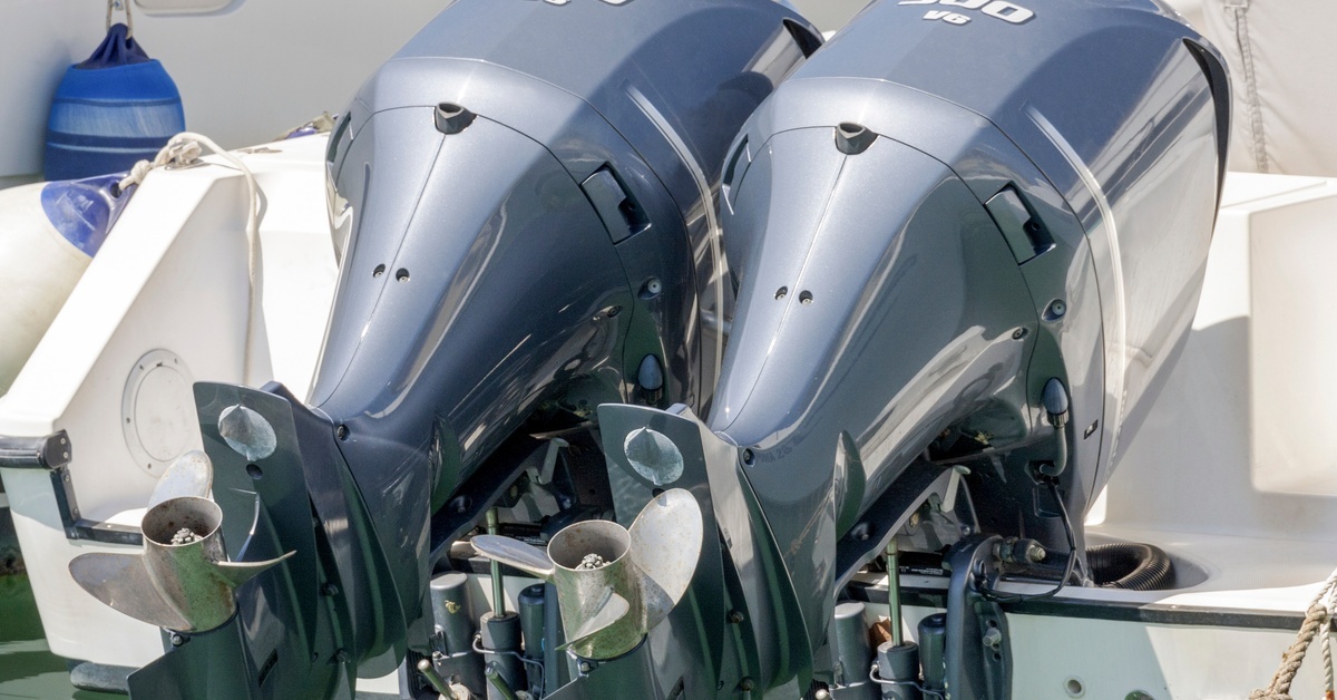 A pair of blue chromed “300 V6” electric outboard engines on the back of a white boat, hovering above the water.