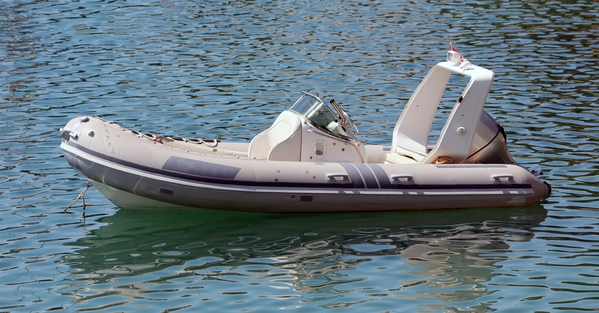 What Makes the ePropulsion Spirit Electric Outboard Unique? A modern grey inflatable boat with an outboard motor sits anchored in a local harbor surrounded by calm blue waters.