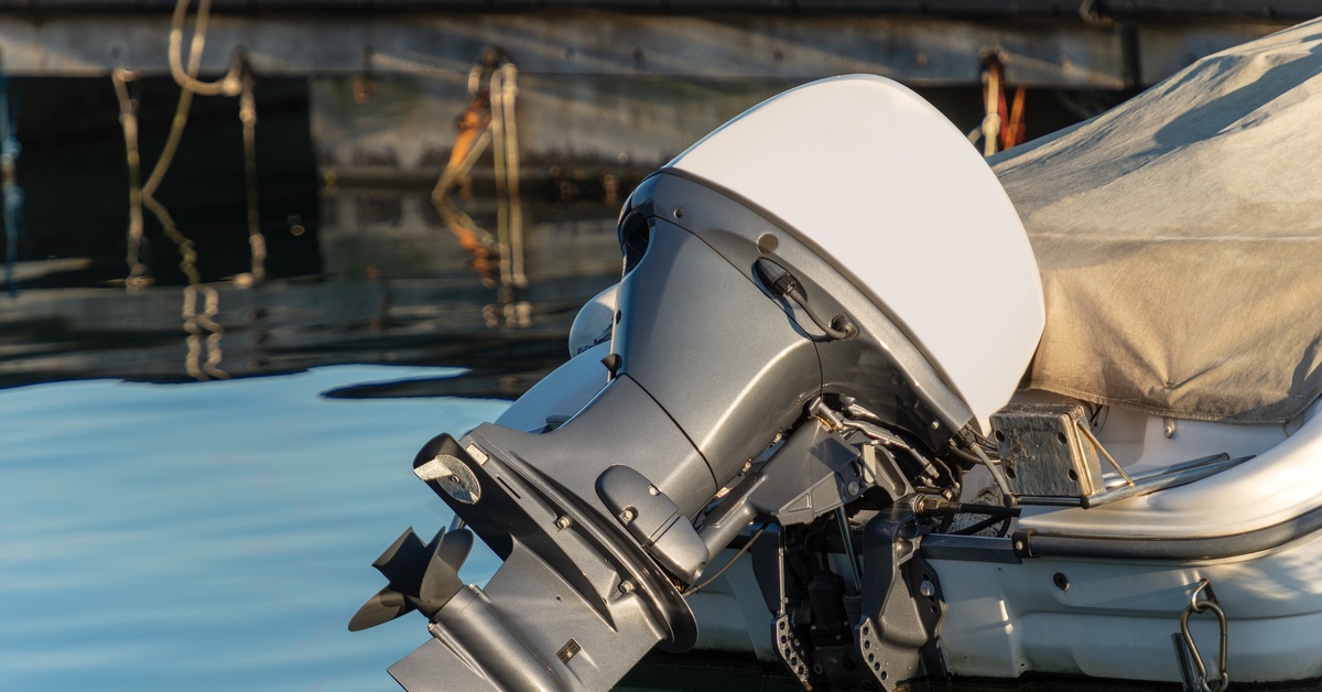 What Causes a Boat’s Outboard Motor To Overheat? A modern outboard motor on a small boat with a fitted cover, docked beside a wooden pier on calm water.