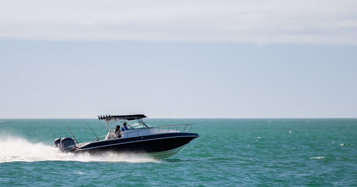 Fuel Stabilizers for Outboards: Do You Really Need Them? A black fishing boat speeding across turquoise waters with water spraying out the back creating a wake. There is a clear blue sky in the background.