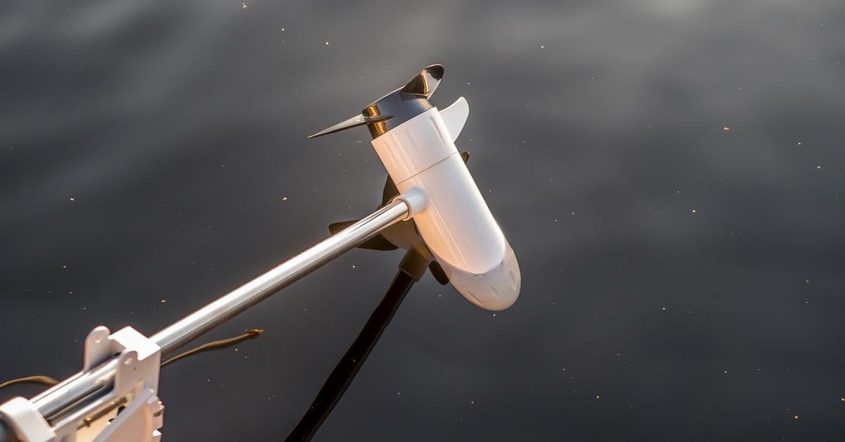 The propeller and motor of a white electric outboard motor mounted on a boat. The propeller is resting slightly above the water. The propeller and motor of a white electric outboard motor mounted on a boat. The propeller is resting slightly above the water.