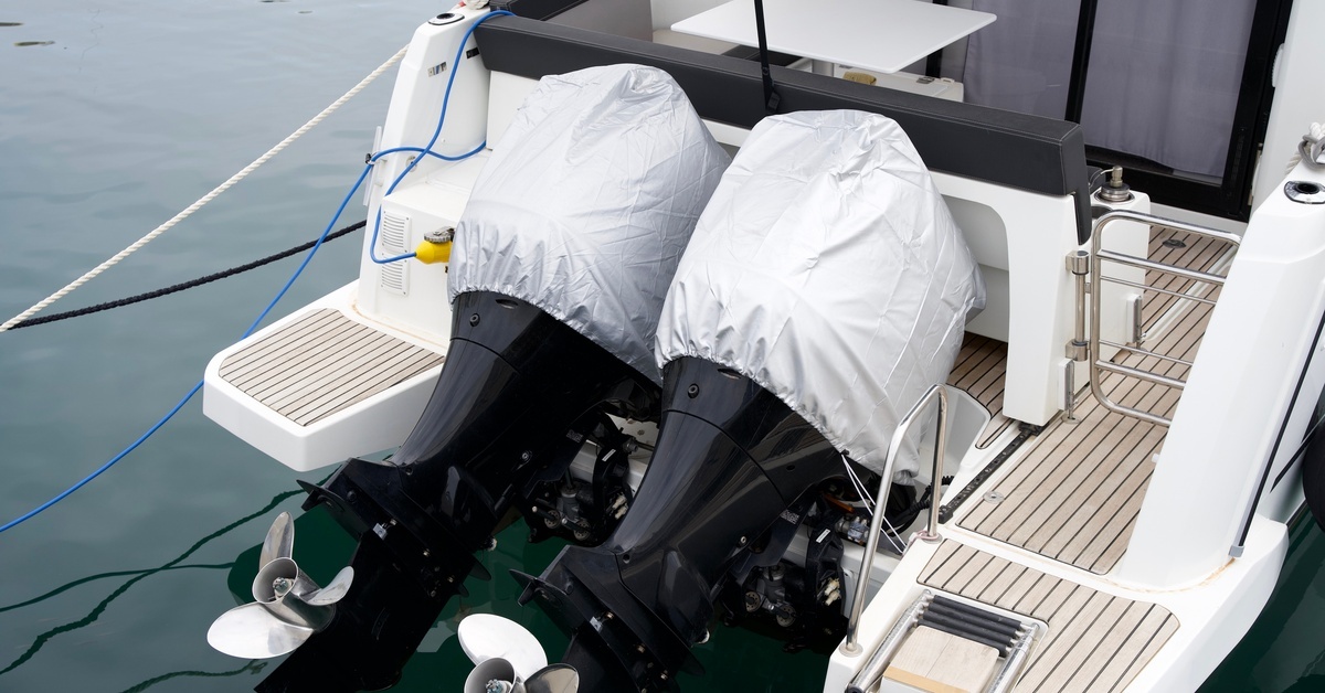 Twin outboard boat motors sit on the stern of a yacht, each covered for protection while the vessel rests on calm dock water. Twin outboard boat motors sit on the stern of a yacht, each covered for protection while the vessel rests on calm dock water.