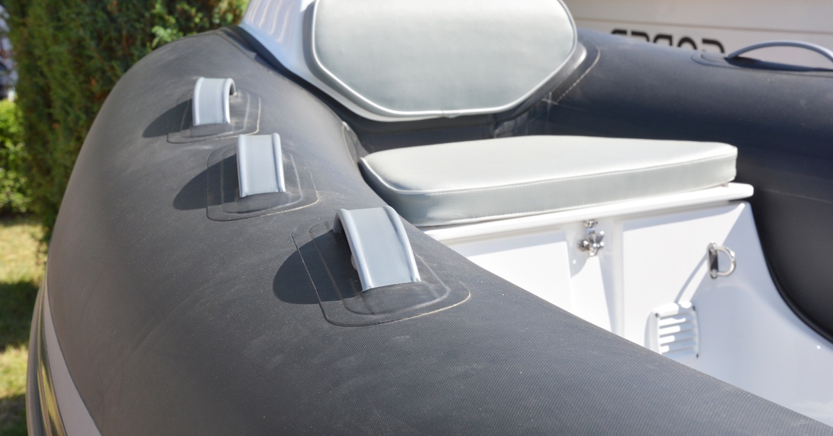 A close-up of one end of a rigid inflatable boat. There is a seat surrounded by the inflatable tube, with handles along the tube. A close-up of one end of a rigid inflatable boat. There is a seat surrounded by the inflatable tube, with handles along the tube.