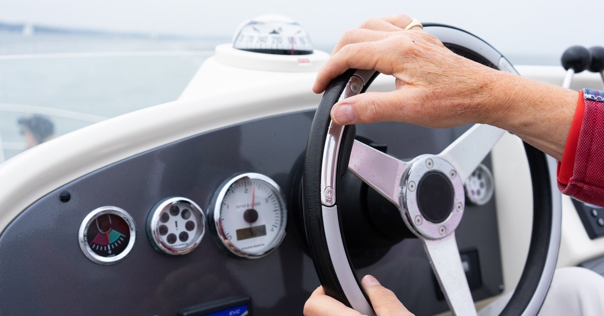 The steering dashboard of a speedboat with someone's hand on the wheel. Several gauges are visible.