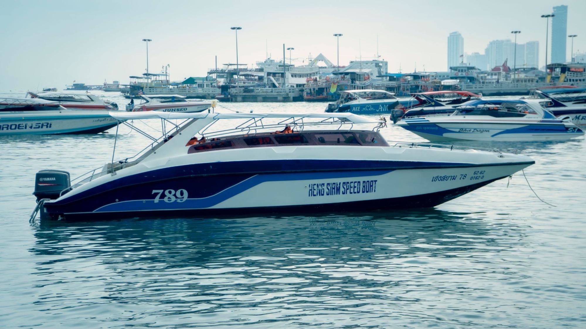 A large white speedboat with blue accents and a Yamaha outboard floats on choppy teal water in a busy harbor.